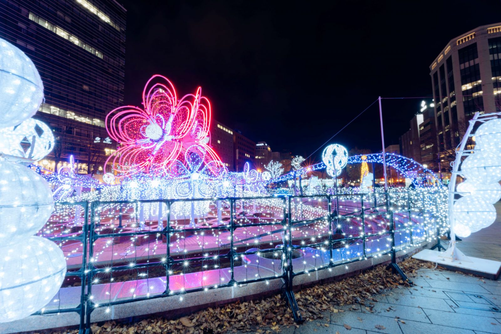 A pink flower-shaped light installation viewed from the side, with white lights extending into the foreground.