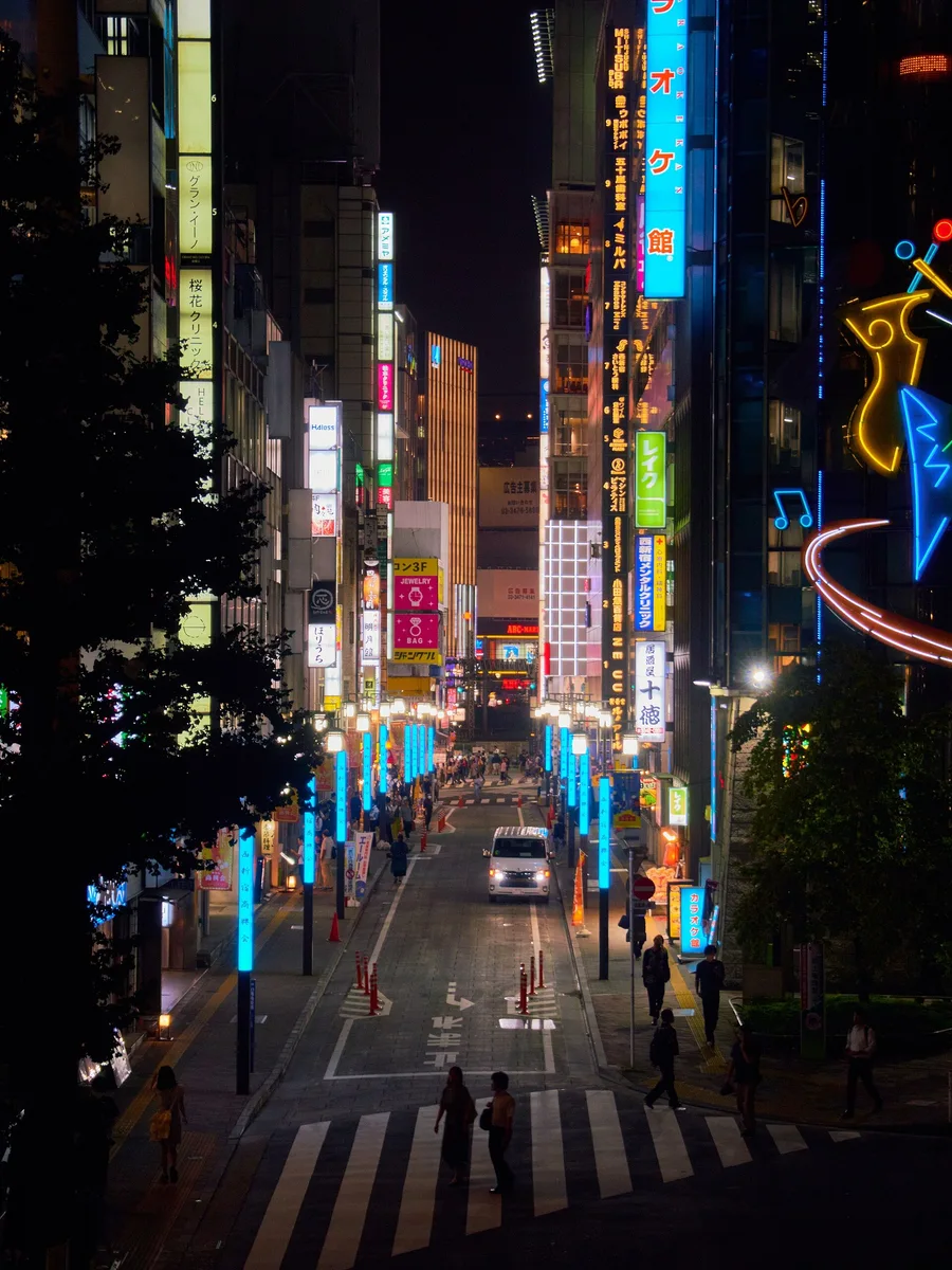 A neon-lit commercial street in Shinjuku at night.